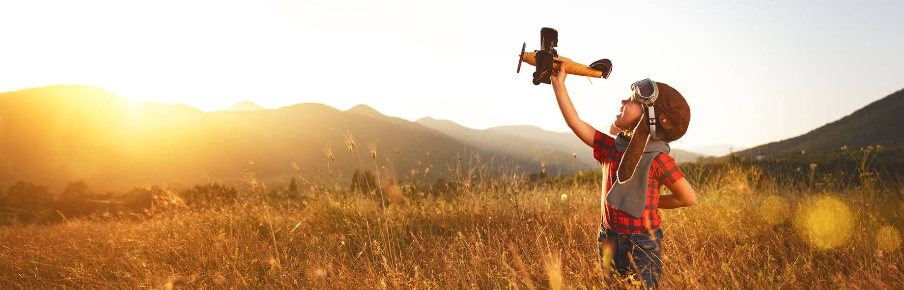 Väike poiss lendurimütsiga lennutab põllul mudellennukit